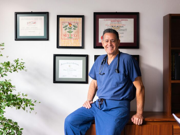 Male doctor in blue scrubs displays diplomas at FQHC clinic