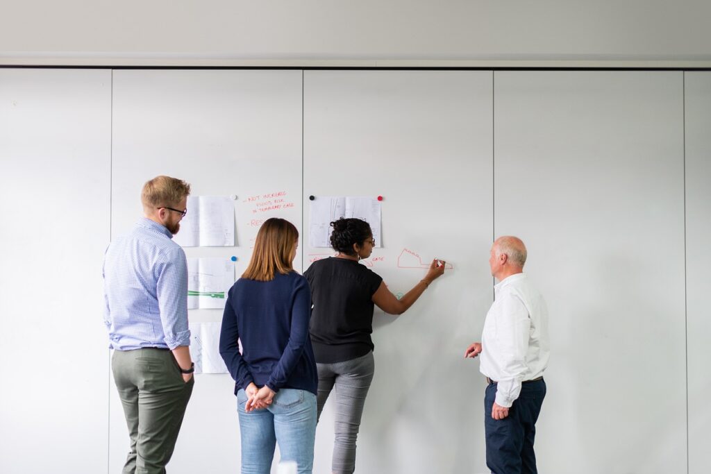 diverse team of healthcare leaders solve a financial problem on a whiteboard.