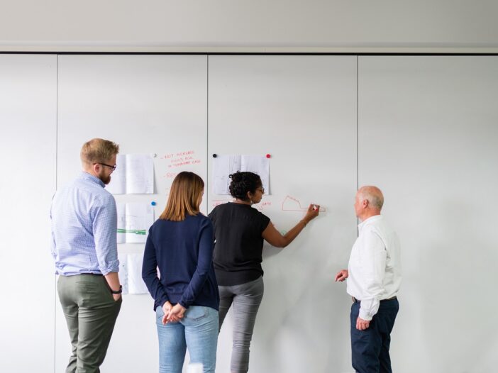 diverse team of healthcare leaders solve a financial problem on a whiteboard.